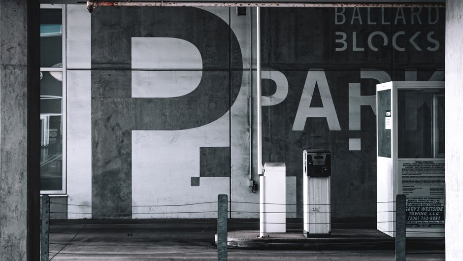 A large, modern wall mural features a bold, black question mark and partial letters on a concrete wall at Ballards Blocks, with a small flower delivery kiosk in front. The kiosk has a white exterior w